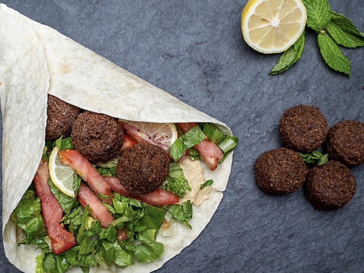 A wrap filled with lettuce, tomatoes, herbs, and falafel sits atop a grey tabletop