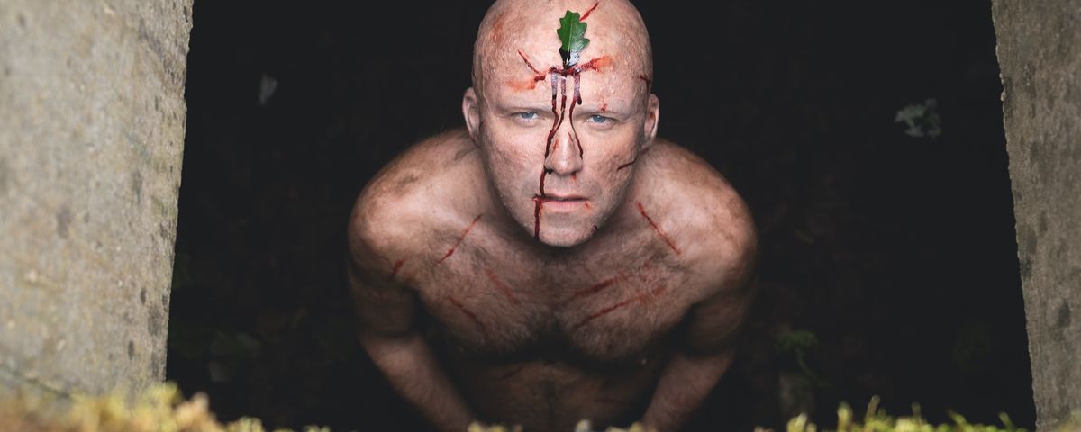Rory Kinnear looks up out of a pit, naked, covered in bloody cuts, and with a leaf on his forehead in Men.