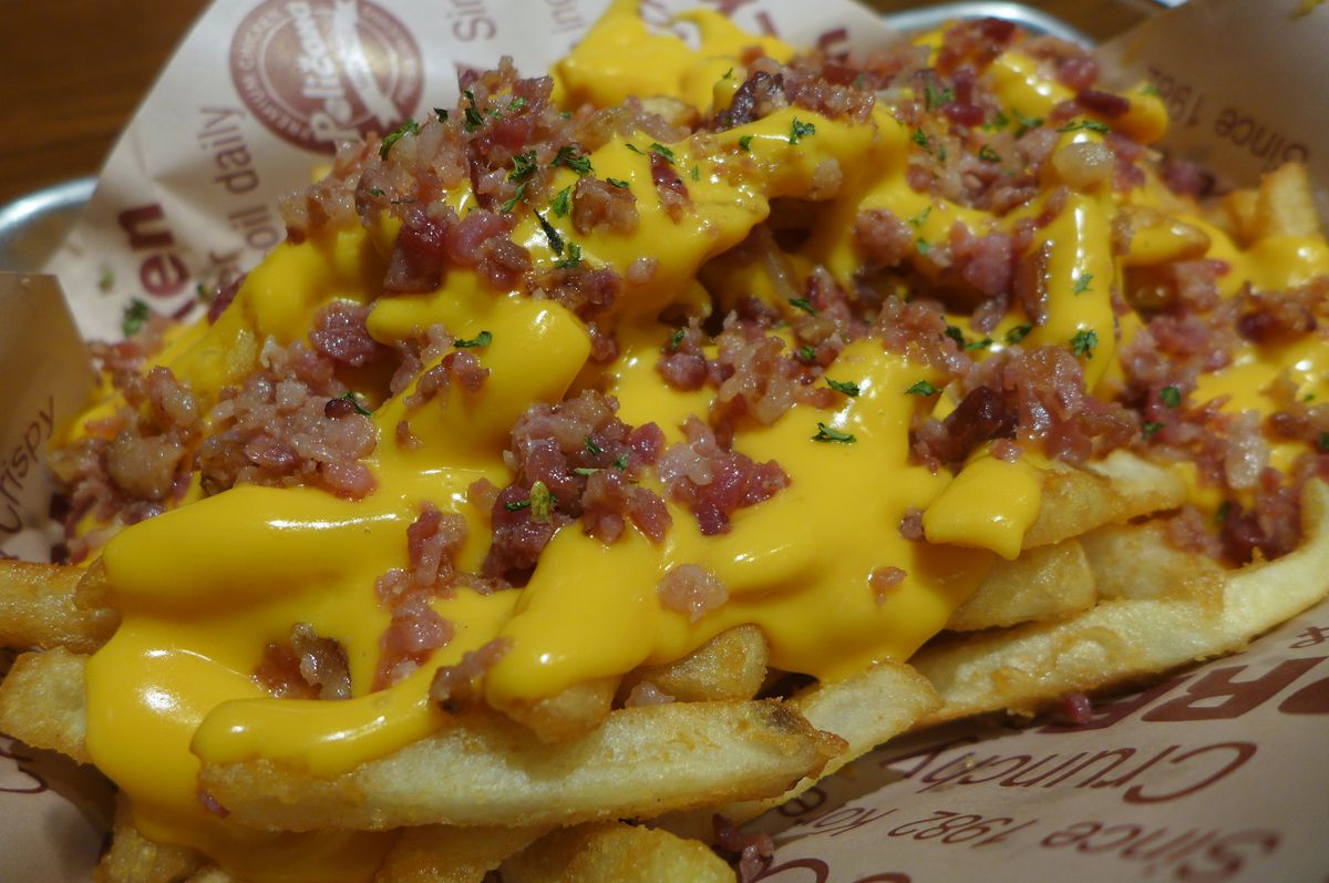 A mass of french fries covered in yellow cheese and bacon.