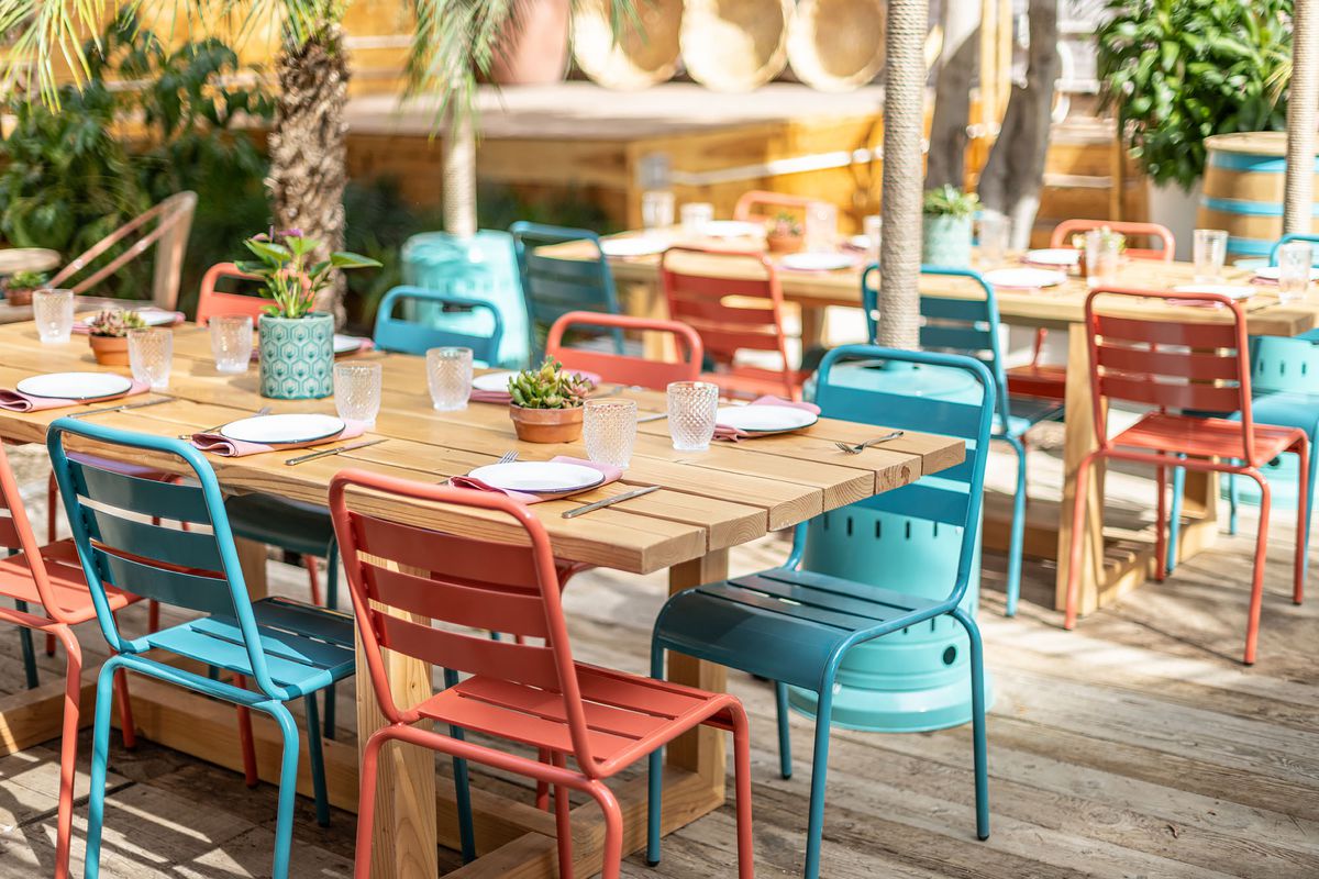 A long table with matching patio chairs over sand at a new restaurant patio.