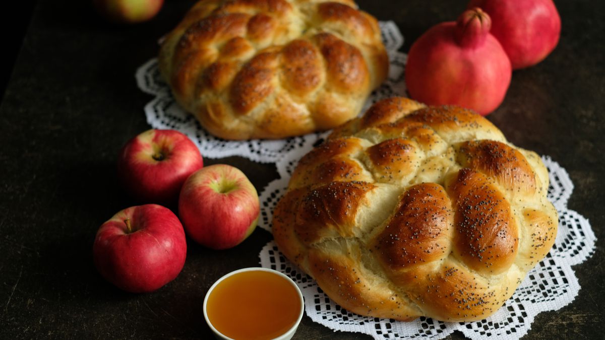 Two crown challah next to apples and a small dish of honey on a black background. 