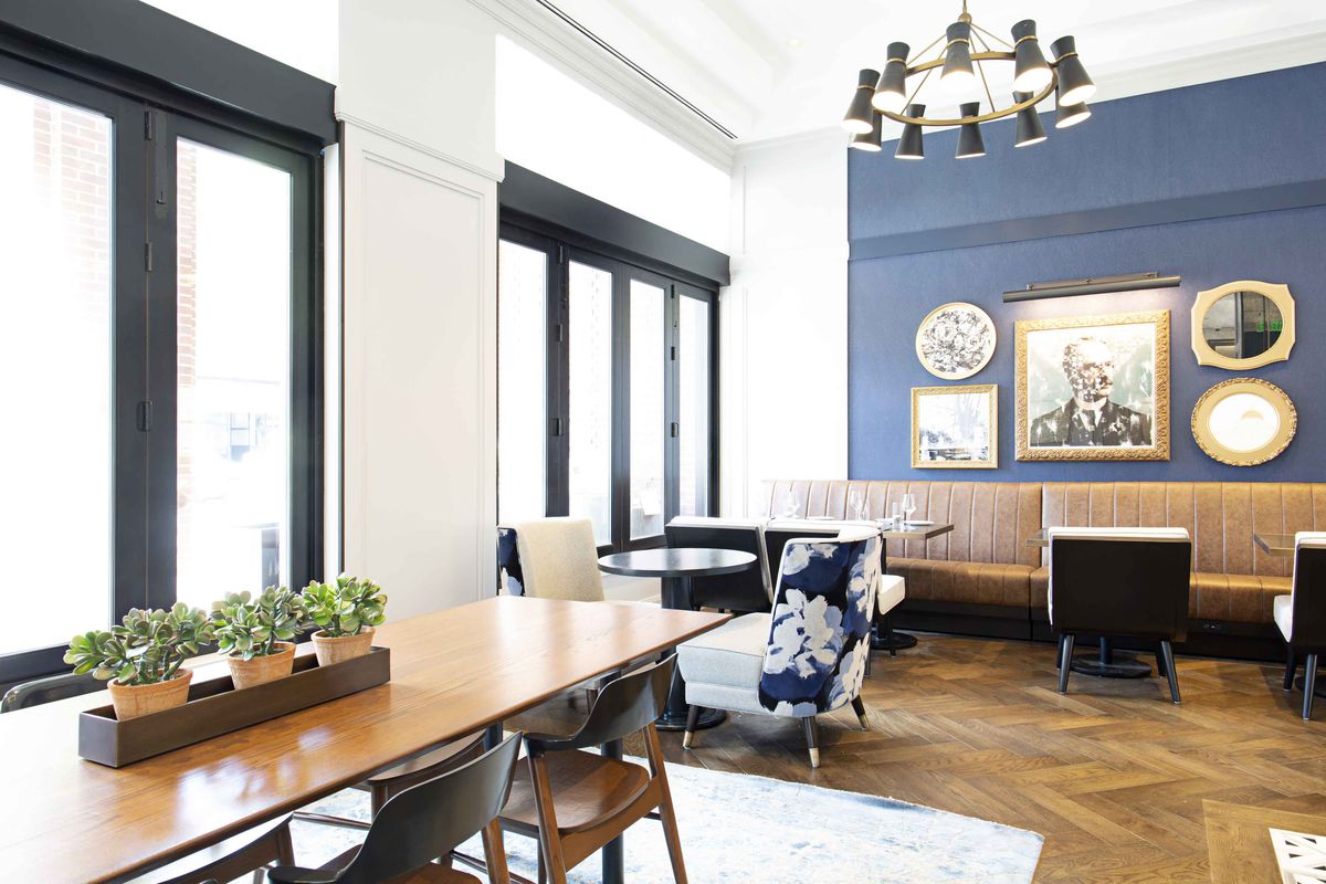 An interior photo of Peregrine in the lobby of the Whitney Hotel in Boston’s Beacon Hill. Nearly floor-to-ceiling windows fill the wall along the street, and a blue wall covered with art is visible in the background.