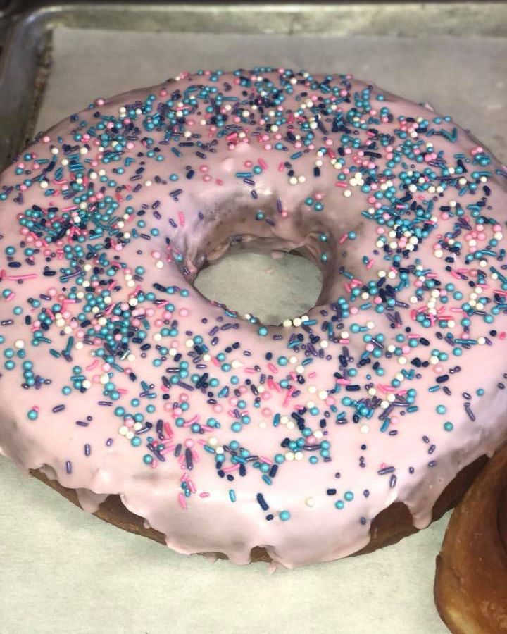 Close-up view of a pink glazed doughnut with nonpareil sprinkles in cool colors of pink, blue and purple.