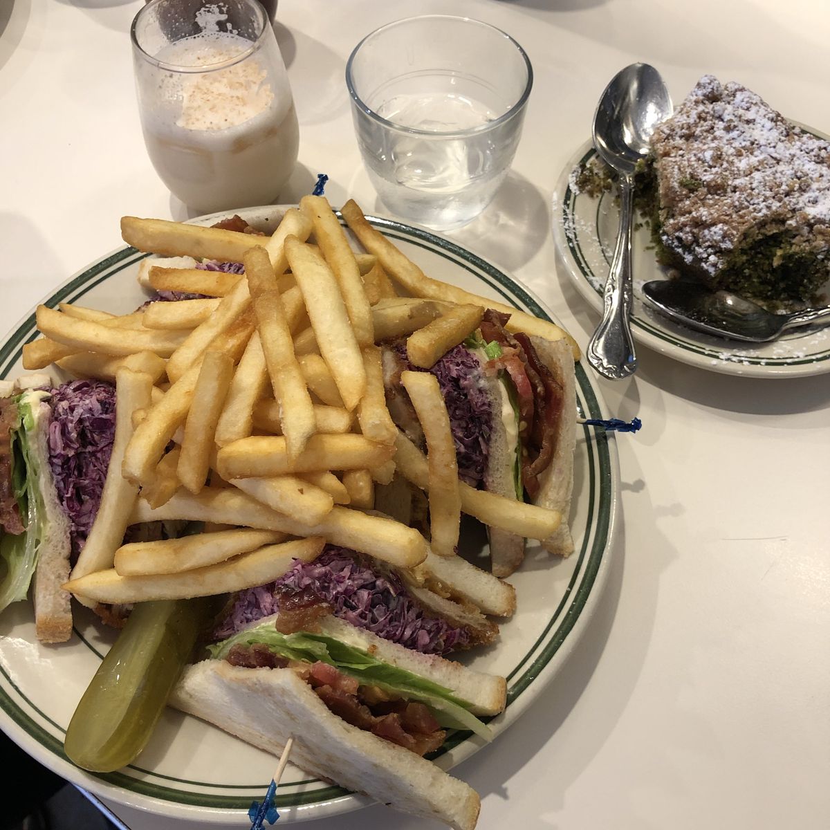 A white plate stuffed with four pieces of a club sandwiches, french fries, and a pickle.