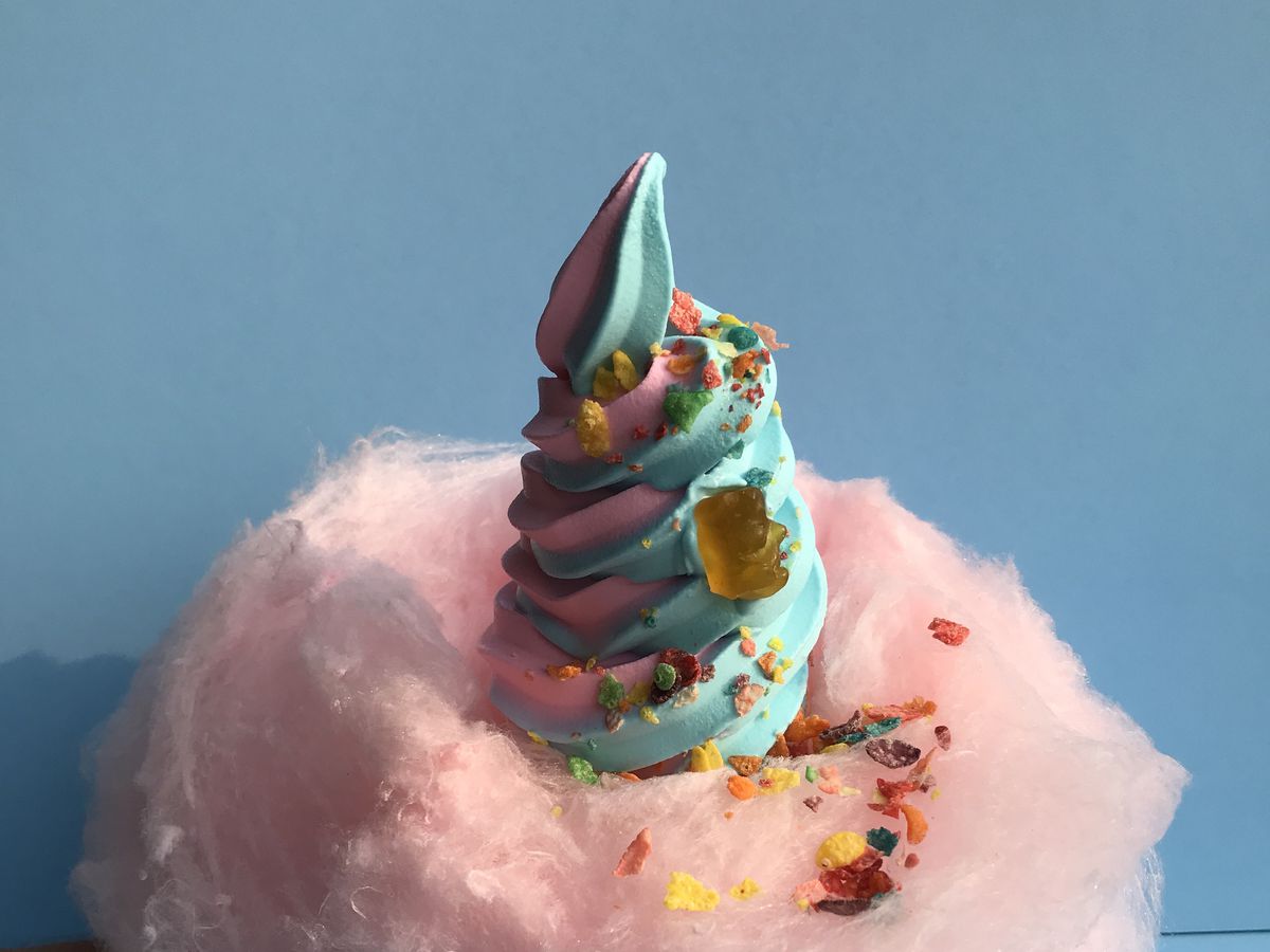 Blue and pink swirled soft serve with a fruity cereal garnish on top of a fluff of pink cotton candy
