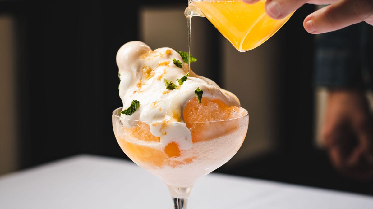 A hand pours an orang liquid over a dessert inside a coupe glass from Nisei in San Francisco.