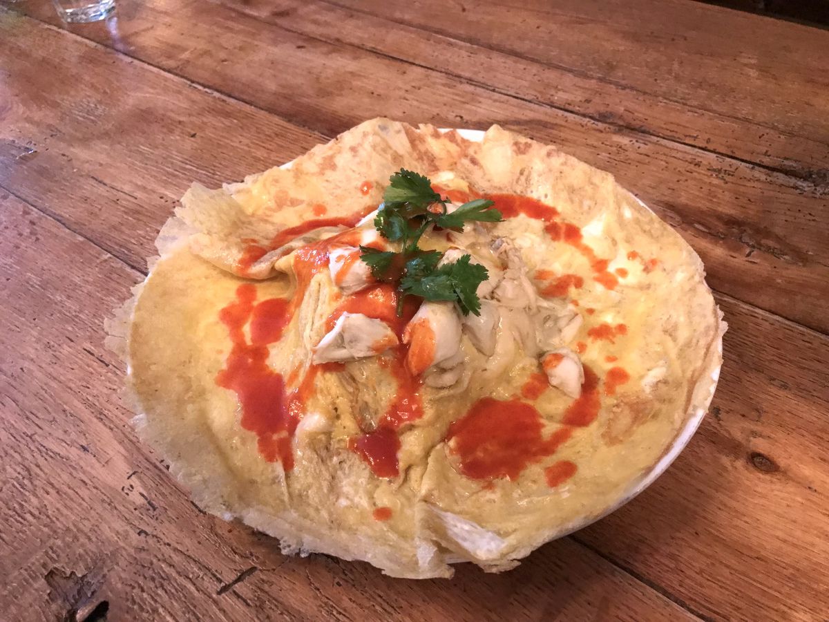 A largeThai-style omelette the size of a plate with crab and dots of hot sauce.