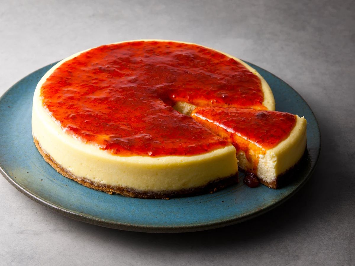 A cheesecake with bright red topping, with a slice hanging out.
