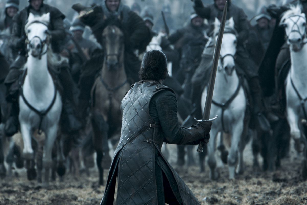 Jon Snow from Game of Thrones stands with a sword in his hands while several men on horses charge at him in the Battle of the Bastards episode