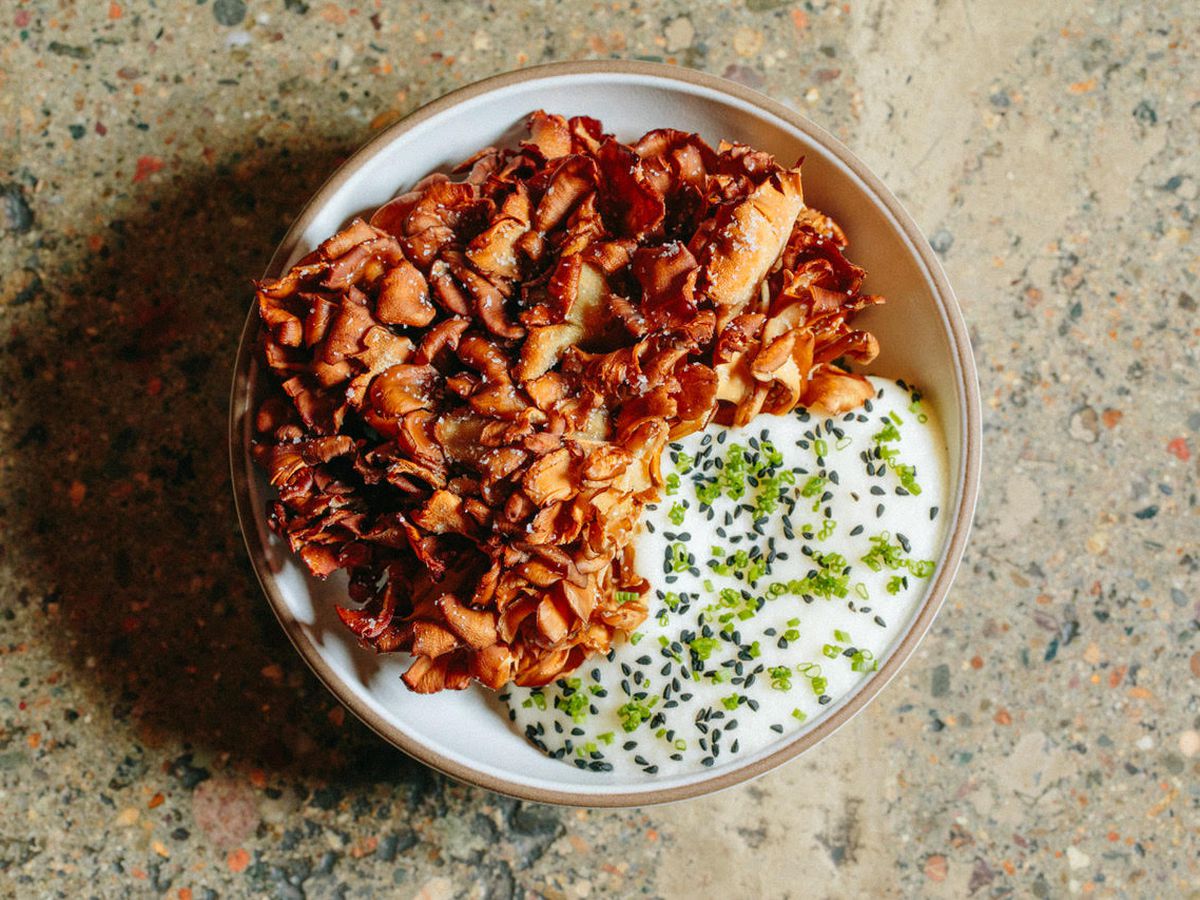 Overhead view of a round bowl full of a bloom of deep-fried hen-of-the-woods mushrooms and a white, herb-filled, foamy sauce