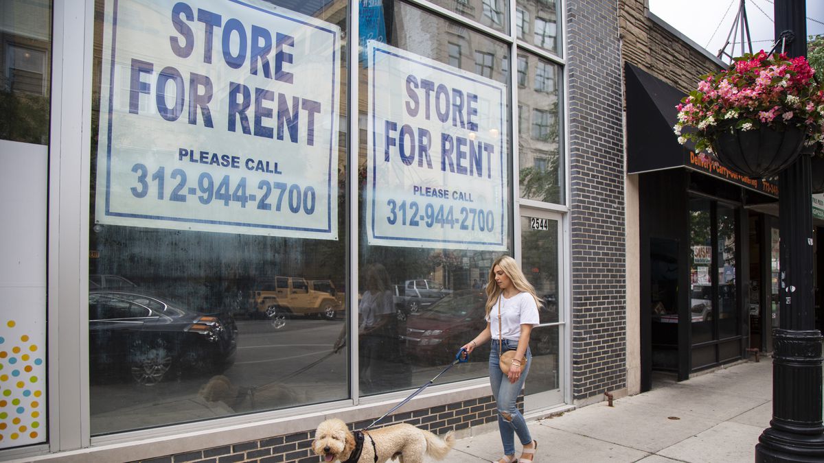 A woman walks her dog past a closed storefront 