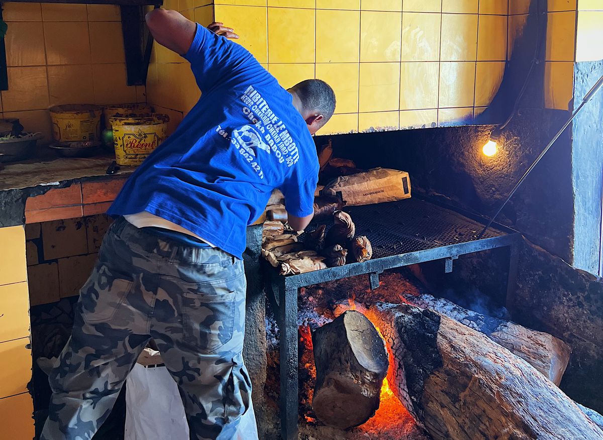 A cook leans into an open hearth.