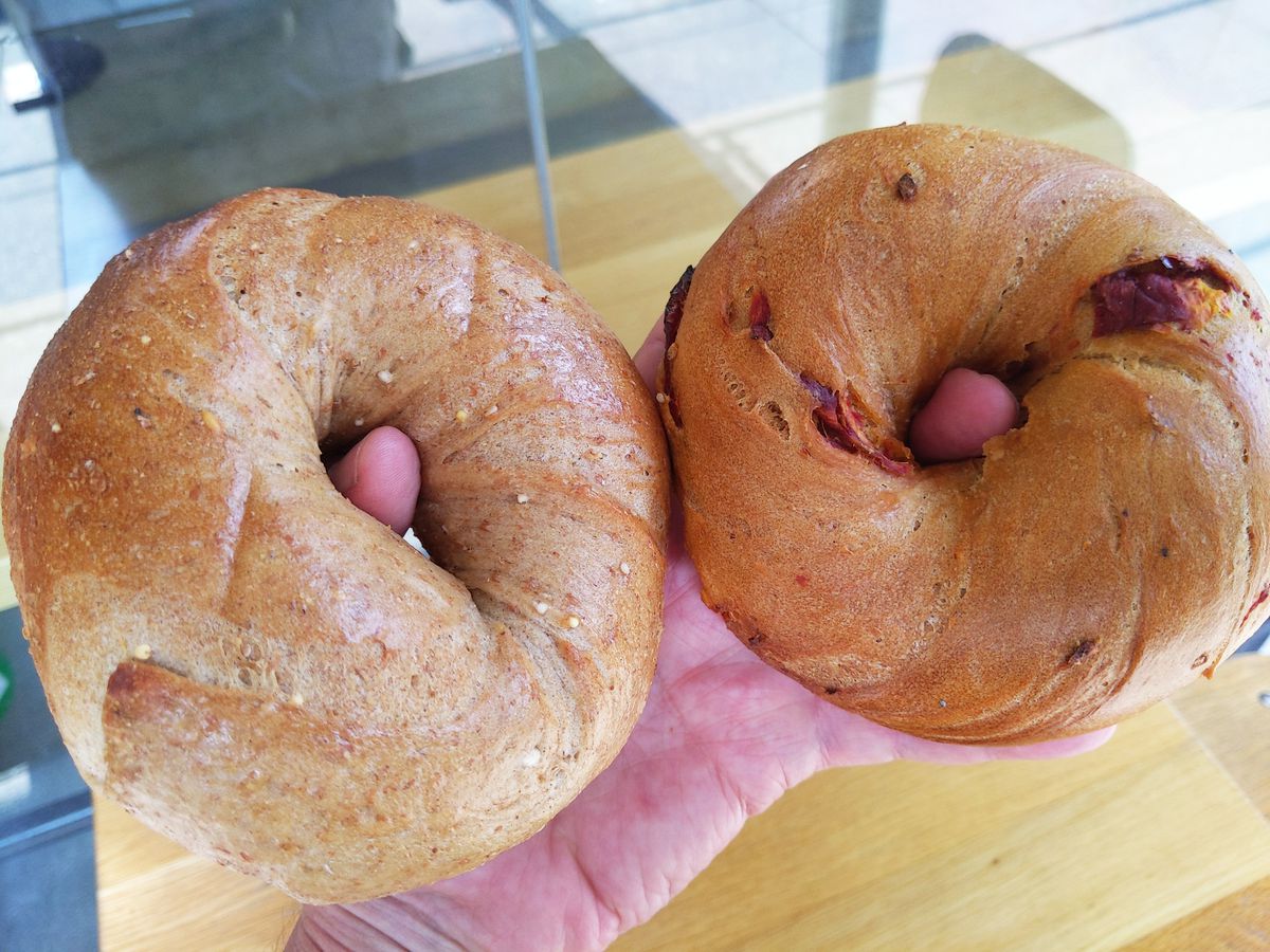 A pair of bagels held in two hands with thumbs sticking through the holes.