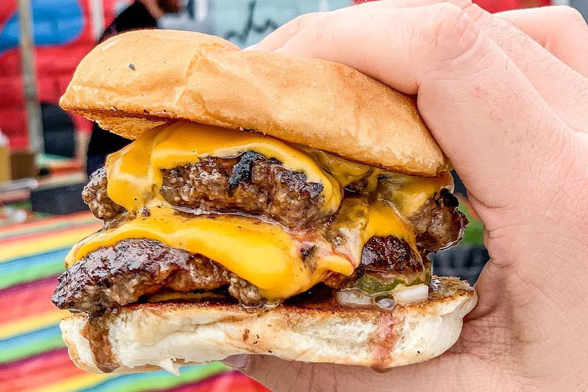 A juicy burger held in a hand as it drops down.