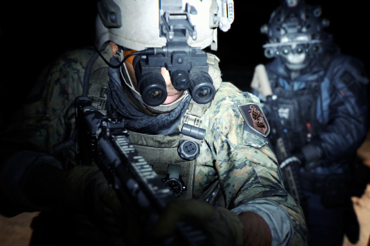 A close-up image of two heavily armed soldiers, wearing night-vision goggles, lit by torchlight at night