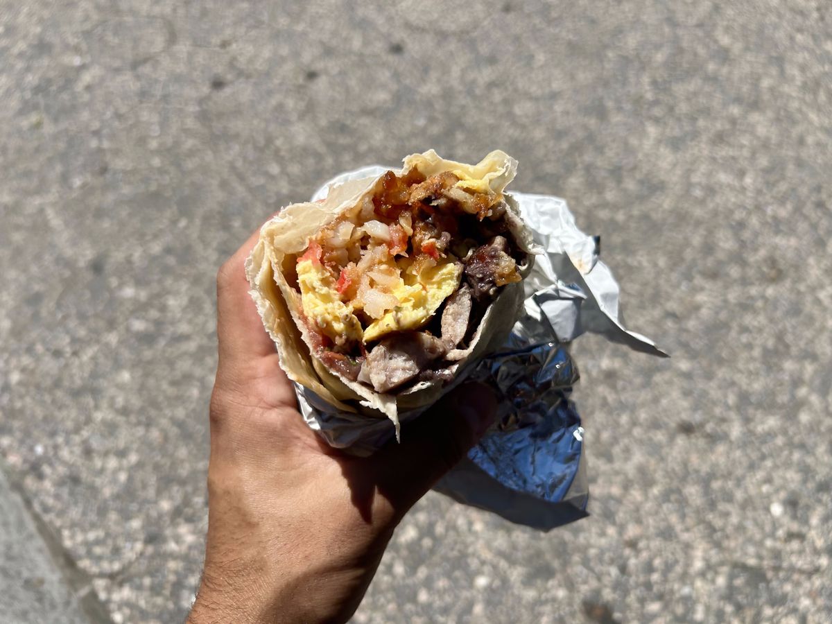 A hand holds up the cross-section of a breakfast burrito with sausage and eggs.