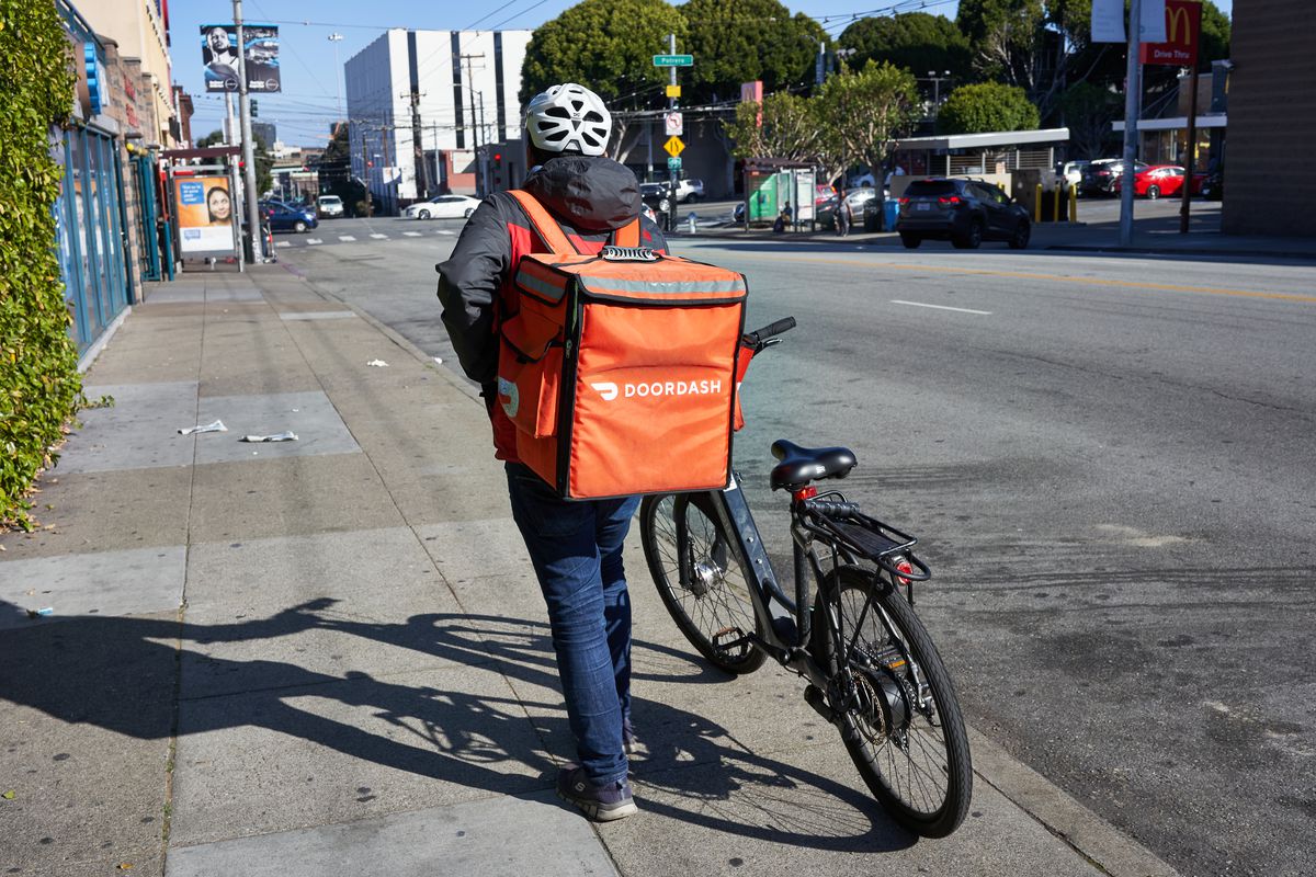 A DoorDash delivery worker walks his bike along the road in the Mission neighborhood of San Francisco, California.