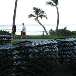 People walk past the Marriott Maui Ocean Club resort in Lahaina, Hawaii, as workers tie down chairs before a tsunami was predicted to hit Hawaii Saturday.