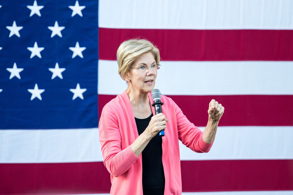 Sen. Elizabeth Warren speaking into a microphone in front of an American flag.