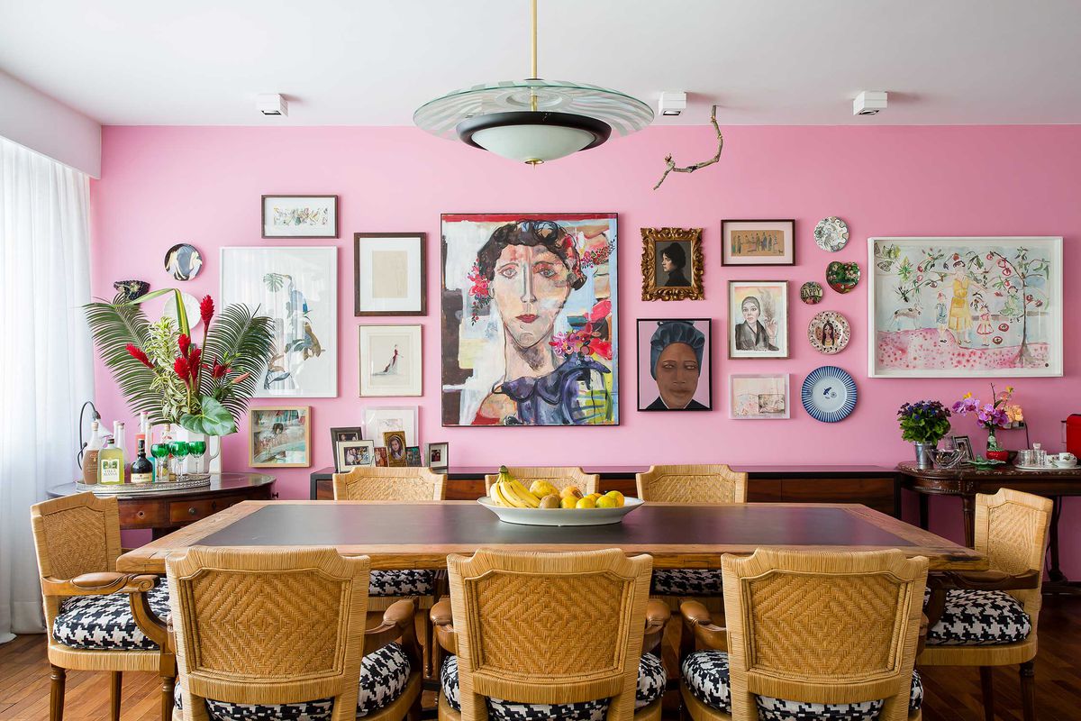 View of large, sunny living room painted white except for a bright pink picture wall at one end by the dining table.