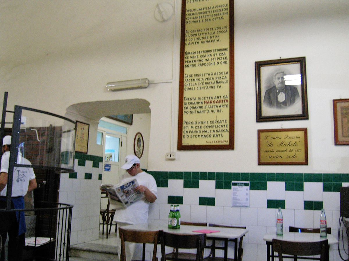 A white tiled room with a man standing in front reading a newspaper.