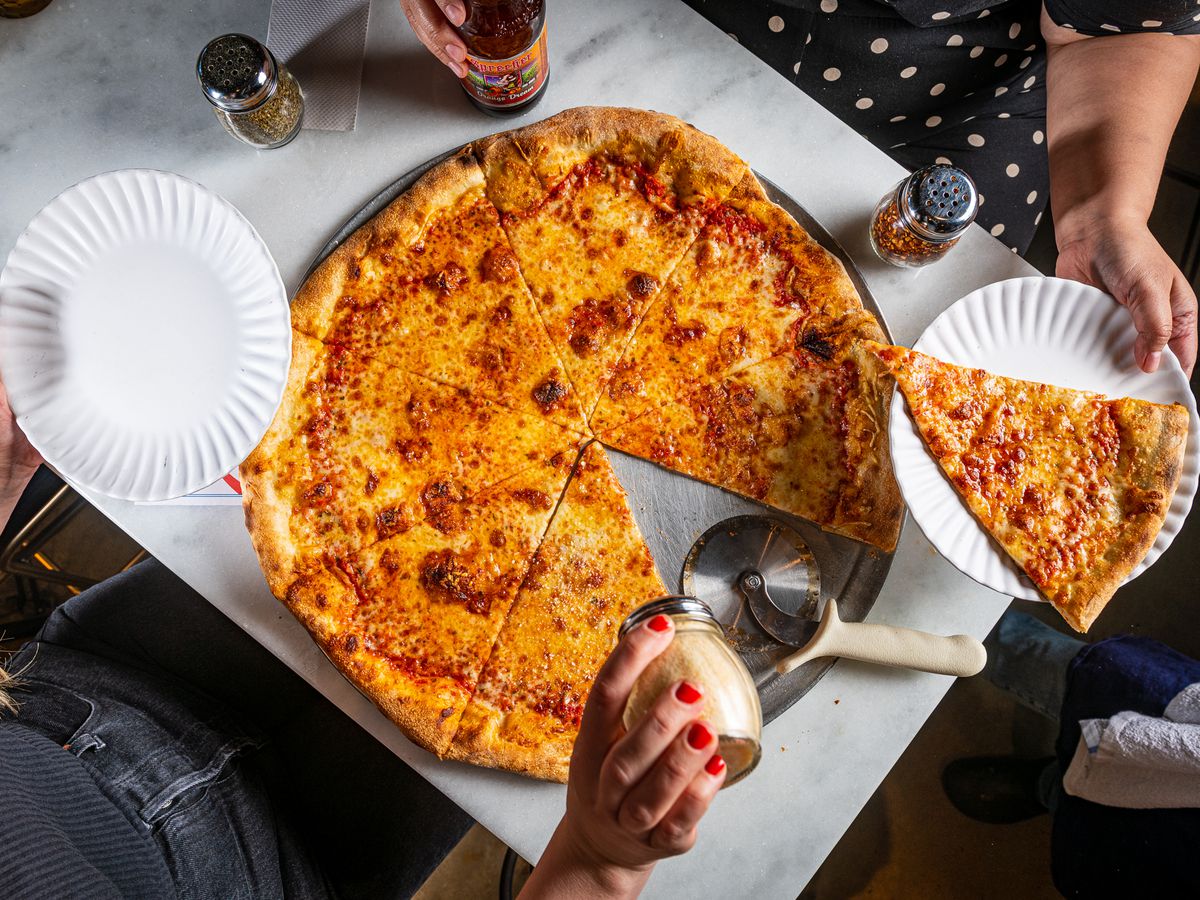 A full pizza with people removing slices.