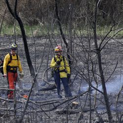 Firefighters work at the scene of a brush fire by the Jordan River in South Jordan on Thursday, April 9, 2020.