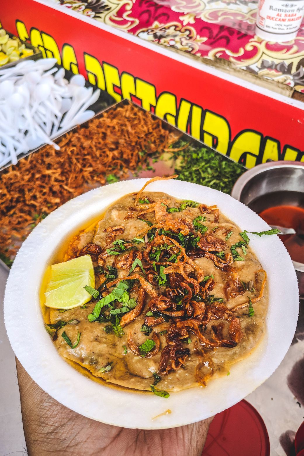 A bowl of haleem topped with fried onions, herbs, and a lemon wedge.