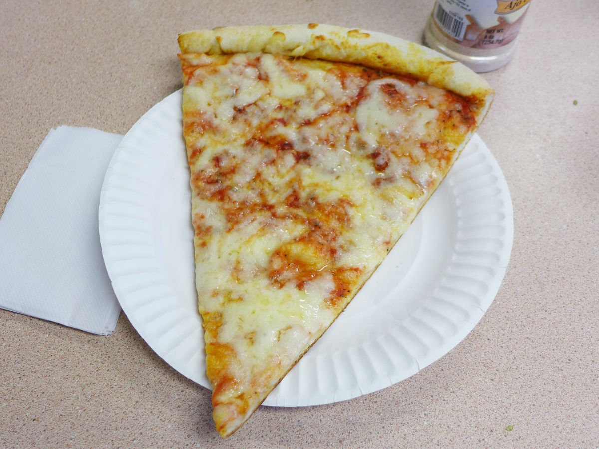 A slice of plain cheese pizza sits on a white paper plate placed on a brown counter.