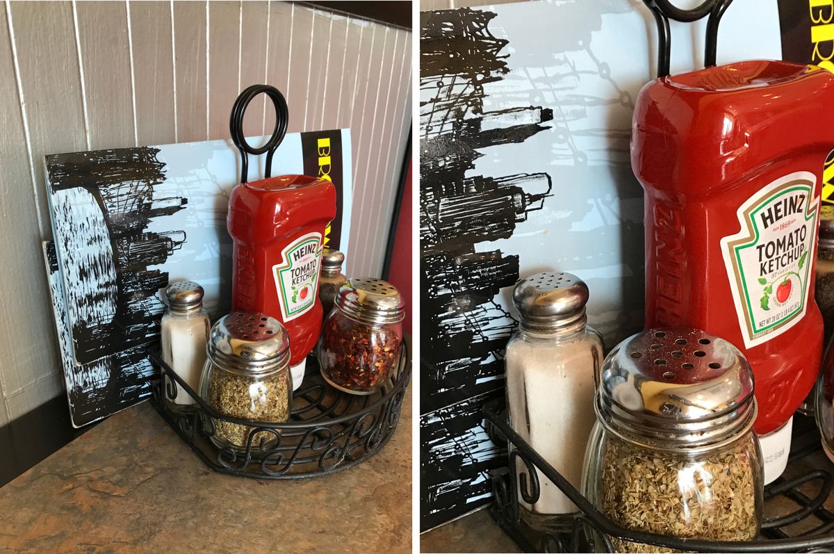 A side-by-side comparison of photos taken with the iPhone 7. On the left, a table with a caddy containing ketchup, salt, oregano and hot peppers. On the right, a closer version of the same image in which the flecks of oregano are sharply visible. 