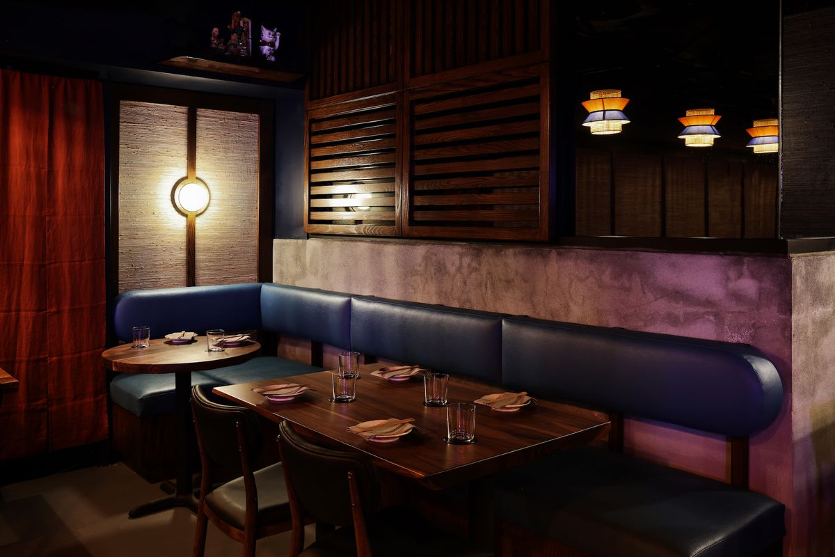 A dark dining room with blue booth seating and deep wood cafe tables at an evening restaurant in Los Angeles.