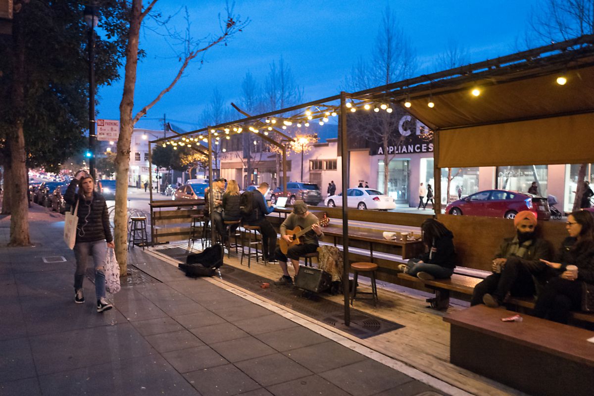 People walk past a public parklet where a street musician performs on Valencia street in the Mission District.