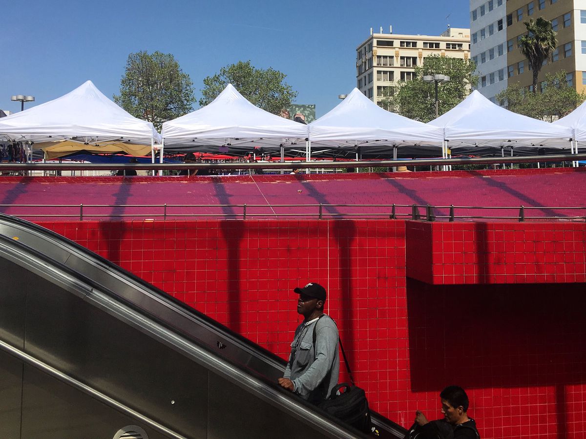 A photo of a man riding an escalator out of the Westlake/MacArthur park subway station, with a wall of red tile in the background. 
