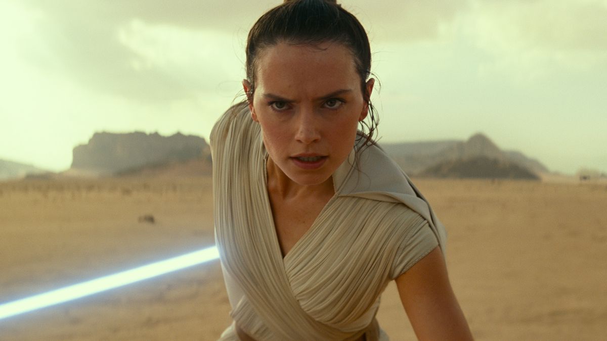 rey stands in a battle stance with luke’s lightsaber