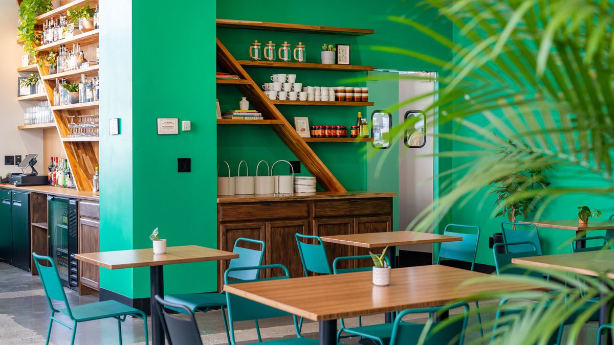 The dining room of a restaurant, with green walls and a shelf of pantry goods.