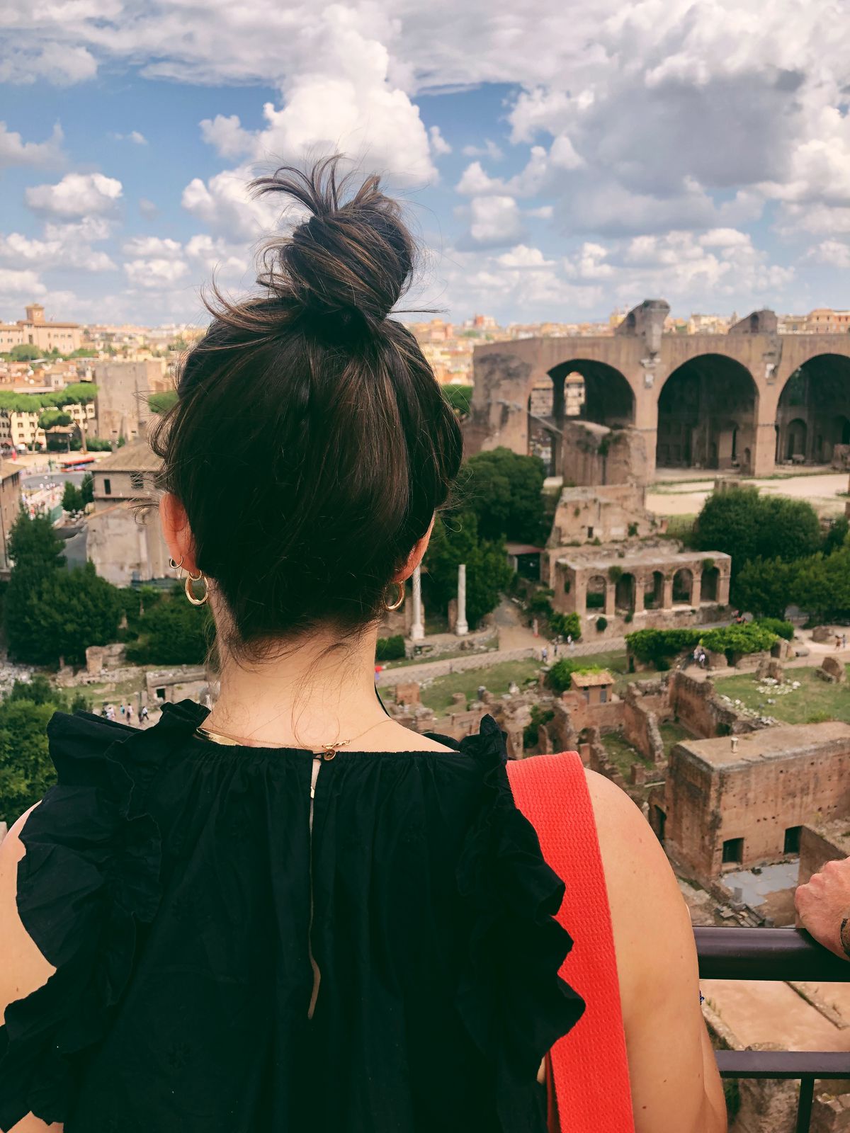 A woman with her back toward the camera looks out into architectural ruins.