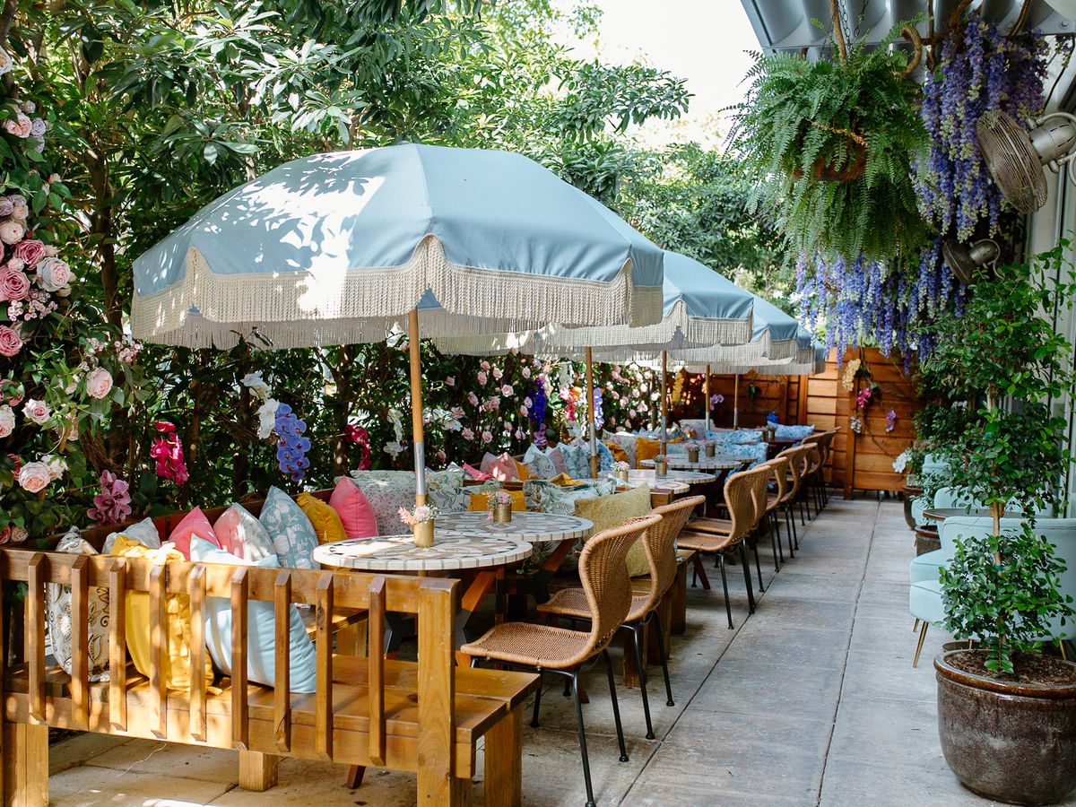 A patio with a long table shaded by white umbrellas and surrounded by florals.