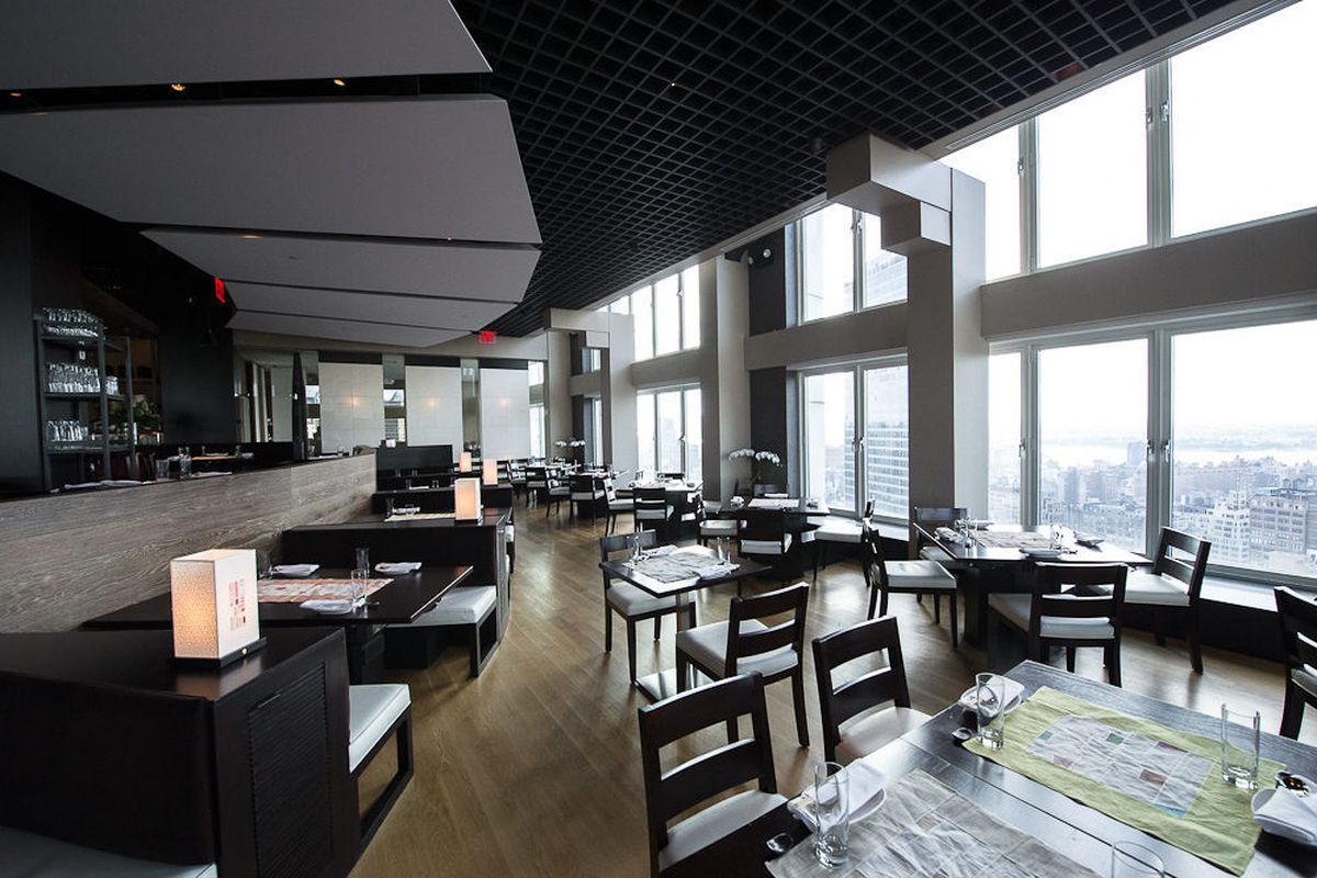 A spacious dining room is well-lit by natural light, with help from floor-to-ceiling windows that offer sweeping views of the city