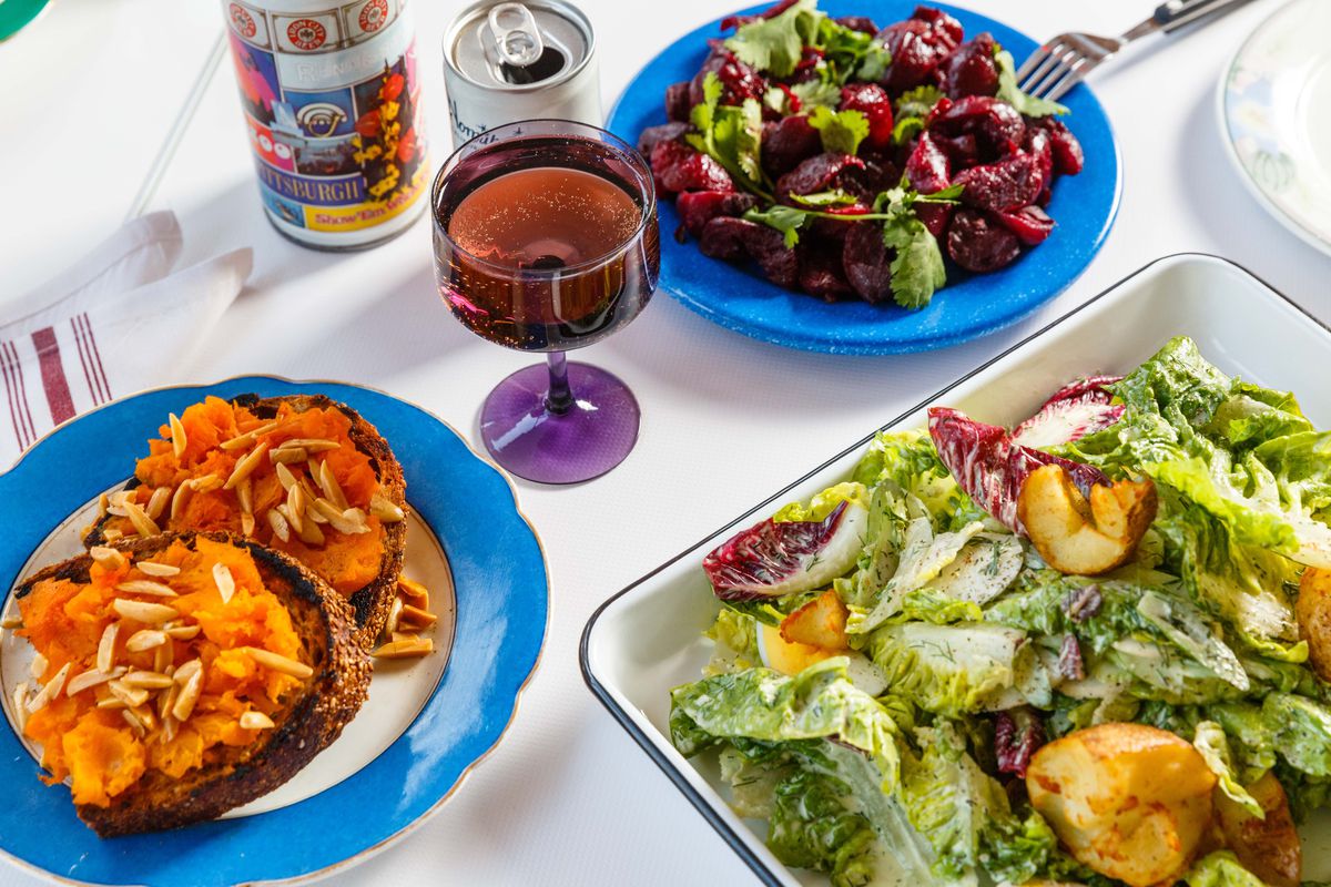 Squash toast and salad on colorful plates spread across a white table at Gertie
