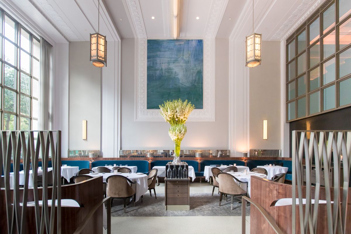 A high-ceilinged, elegant dining room with a blue painting hanging in the back.