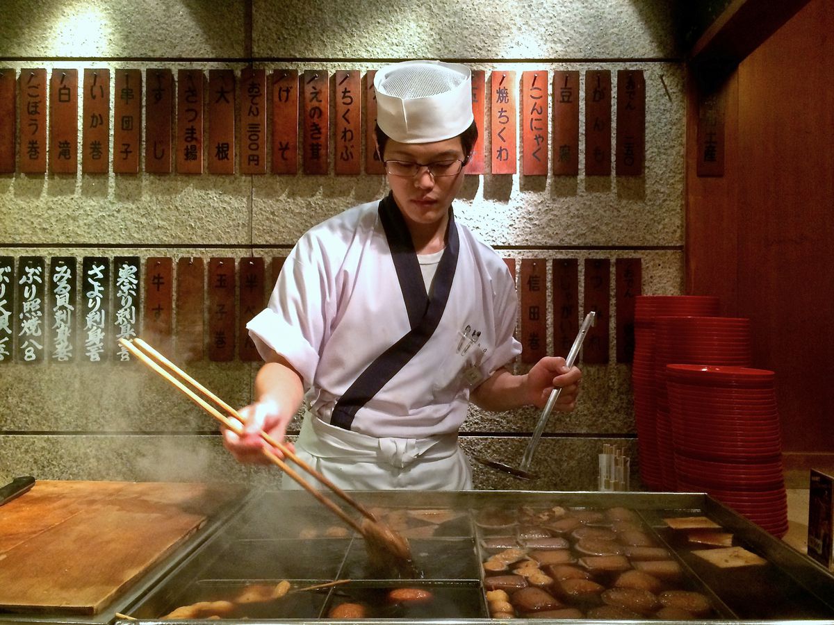 A chef uses long chopsticks to move meat on a grill.