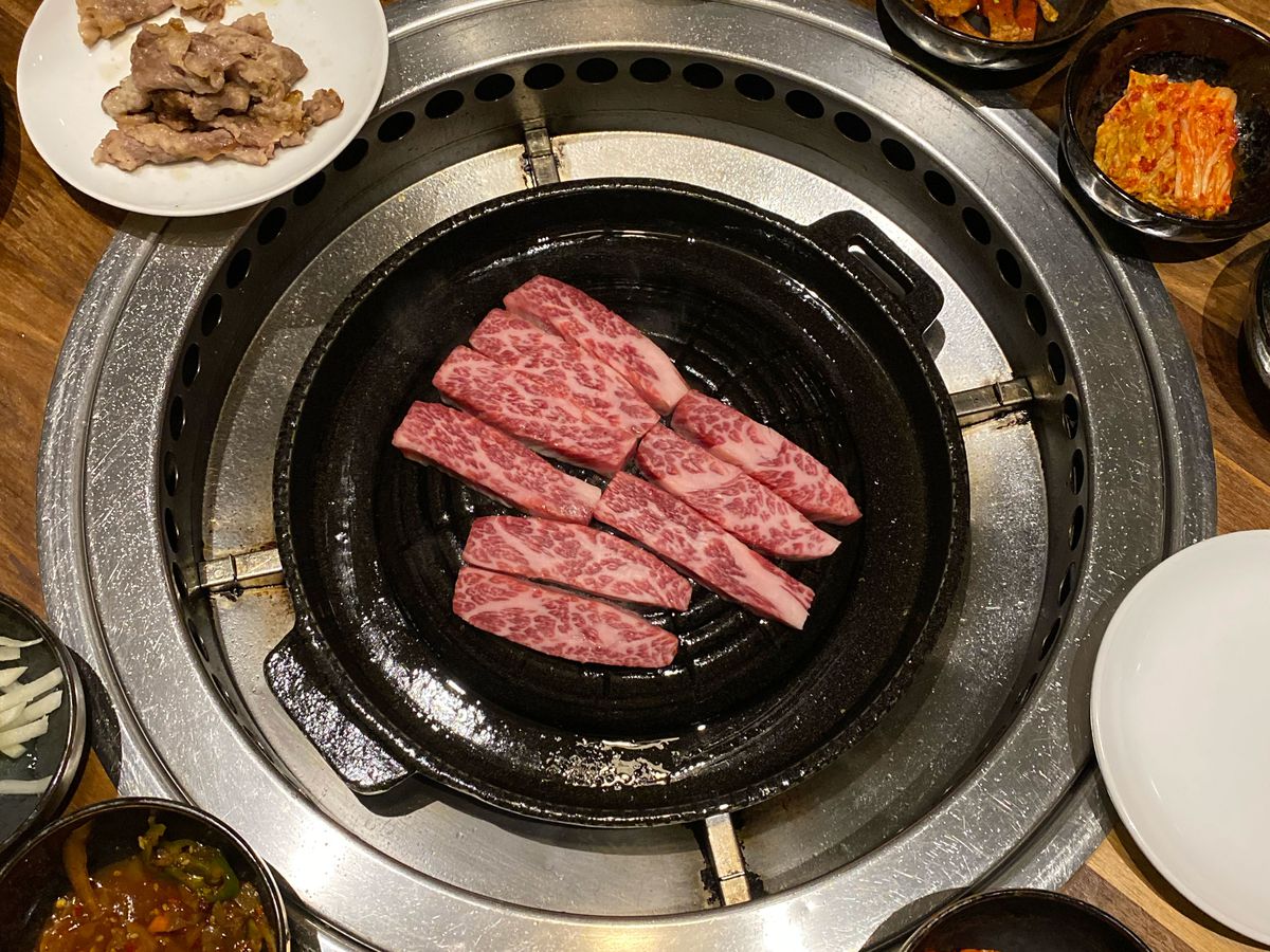 A grill in the middle of the table with strips of pink meat laying on top and white small plates to the sides.