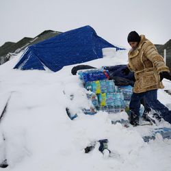 In this Tuesday, Nov. 29, 2016 photo, Lawrence Valdez, of New Mexico and a member of the Chiricahua Apache Native American tribe, drops off bottles of water at the Oceti Sakowin camp where people have gathered to protest the Dakota Access oil pipeline, in Cannon Ball, N.D. Camp dwellers are getting ready for the hardships of a long stay. Mountains of donated food and water are being stockpiled, as is firewood, much of which has come from outside of North Dakota, the least-forested state in the nation. 
