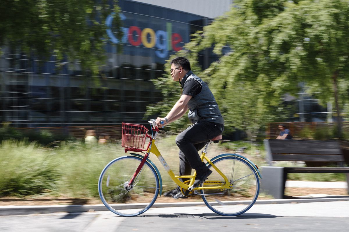 A person rides a bike past signage on the Google campus.