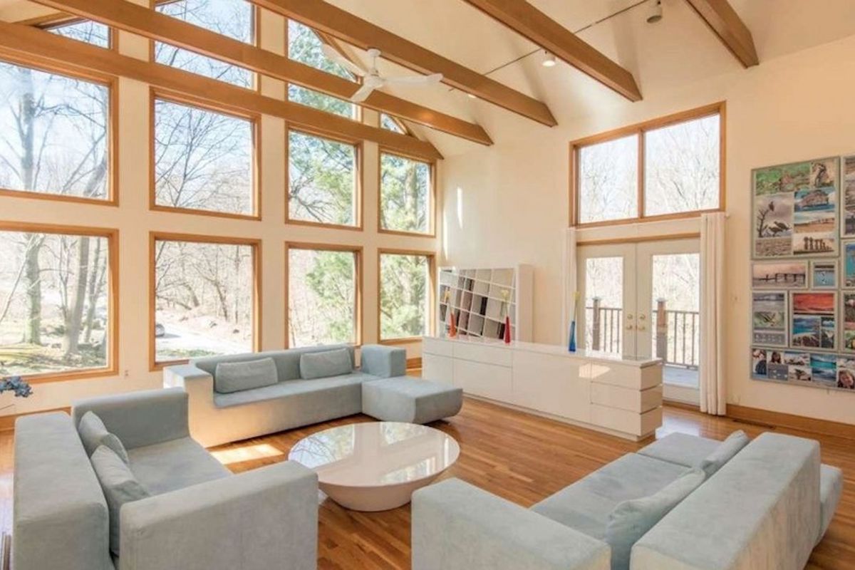 A large two-story living space with exposed beams, hardwood floors, and a wall of windows.