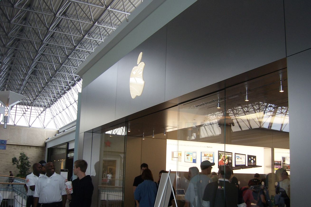 Apple Store front in mall with lit apple logo on top and many people inside