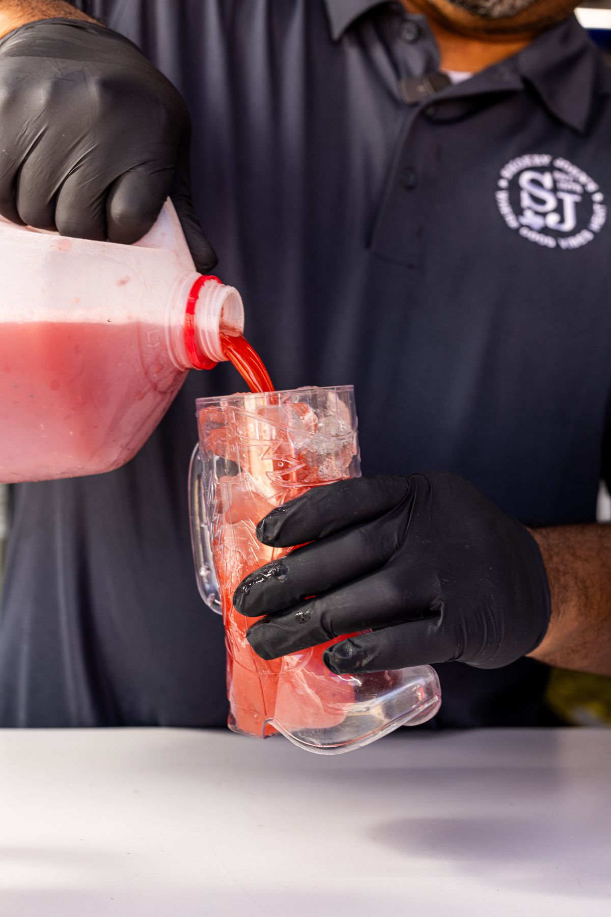 A man pours a red beverage into a clear plastic glass shaped like a cowboy boot that is filled with ice.