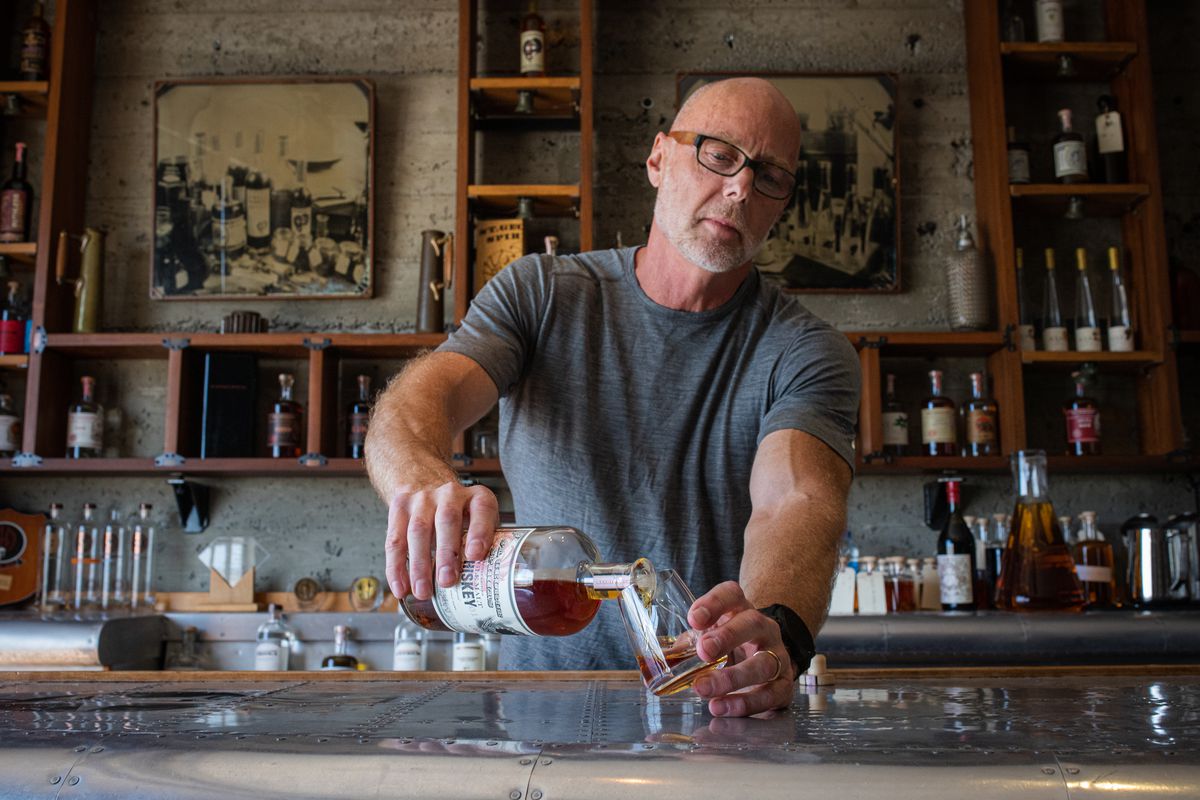 Lance Winters stands behind a bar and pours whiskey into a glass.