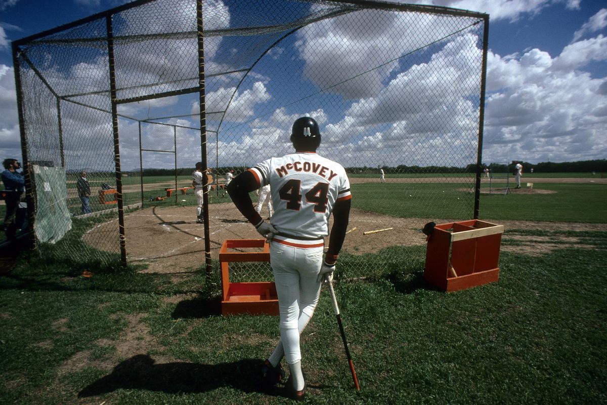 Willie McCovey standing on the field, leaning on his bat, behind the cage for batting practice