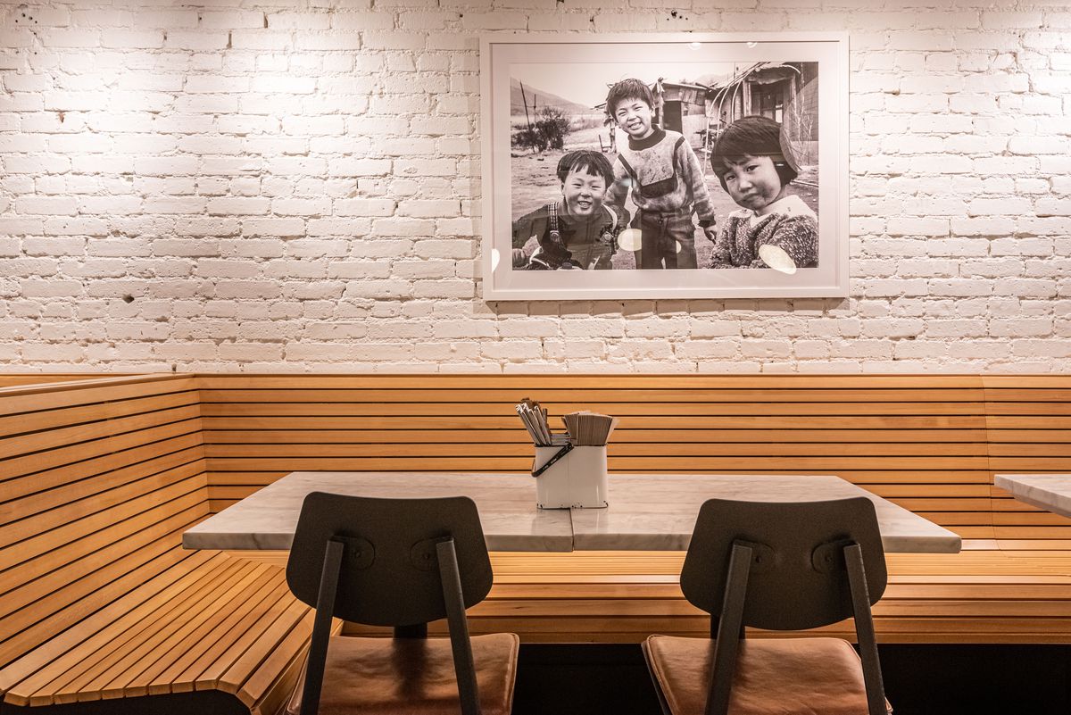 A wooden booth with marble table and white painted brick beneath a family photo inside a restaurant.